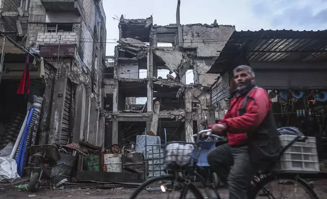 A man cycles past a building that was damaged by airstrikes during the Assad rule in Douma, on the outskirts of Damascus, Syria, Sunday, Dec. 29, 2024 (AP Photo/Ghaith Alsayed)