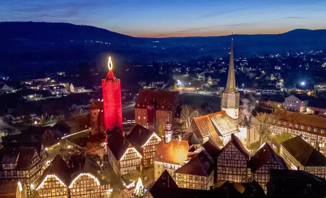 A 42-meter-high candle which is an illuminated medieval tower shines in the historic city centre of Schlitz, Germany, Saturday, Nov. 30, 2024. (AP Photo/Michael Probst)