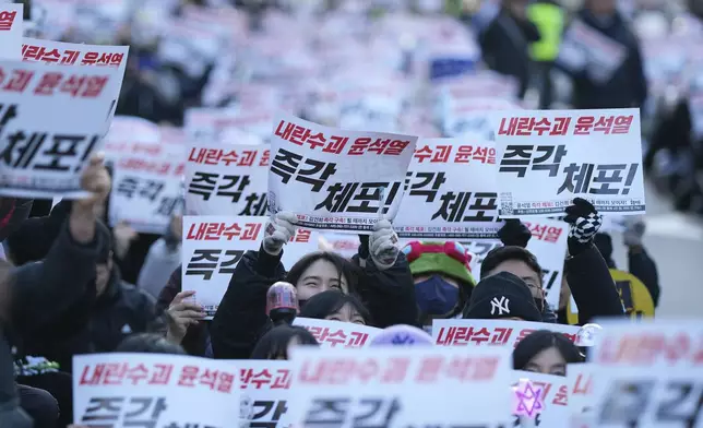 Participants shout slogans during a rally calling on the Constitutional Court to dismiss the President Yoon Suk Yeol, in Seoul, South Korea, Sunday, Dec. 15, 2024. The signs read "Immediately arrest." (AP Photo/Lee Jin-man)