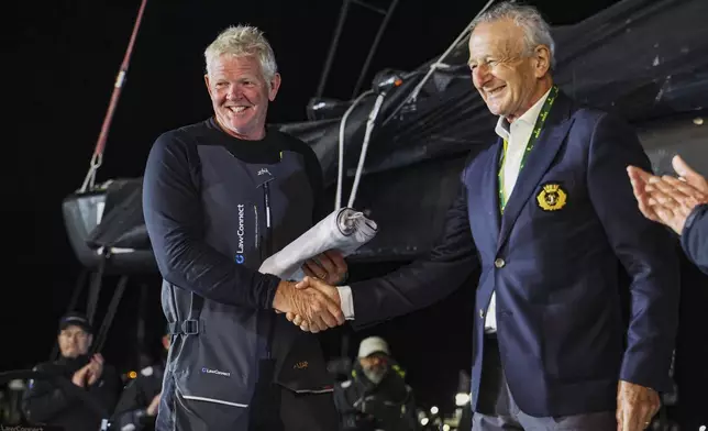 Tony Mutter, left, skipper of Law Connect is presented with the Back Stay flag by Cruising Yacht Club of Australia, Vice Commodore David Jacobs, after winning line honours in the Sydney to Hobart yacht race in Hobart, Australia, Saturday, Dec. 28, 2024. (Salty Dingo via AP)