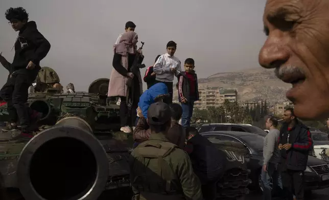 A youth, holding a rifle borrowed from a Syrian opposition fighter people, poses for a picture on the top of a government forces tank that was left on a street, at the Umayyad Square in Damascus, Syria, Wednesday, Dec. 11, 2024. (AP Photo/Leo Correa)