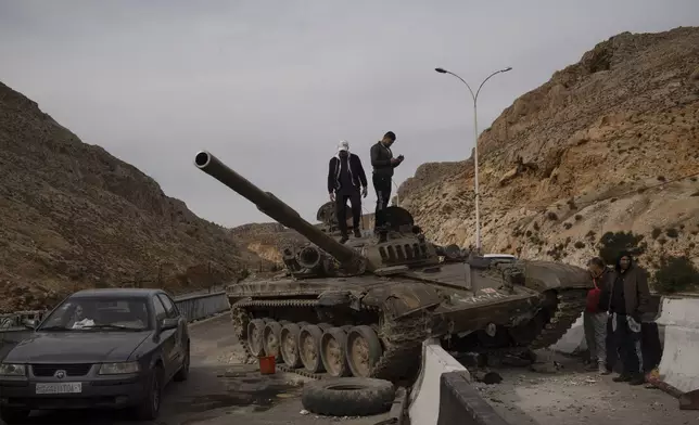 Syrians stand on the top of a government forces tank that was left on a road, on their way to Damascus, Syria, Wednesday, Dec. 11, 2024. (AP Photo/Leo Correa)