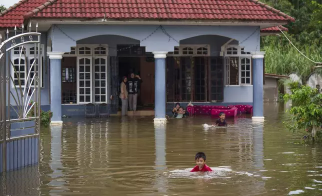 Children wade through flood water outside their home in Tumpat, outskirts of Kota Bahru, Malaysia, Tuesday, Dec. 3, 2024. (AP Photo/Vincent Thian)