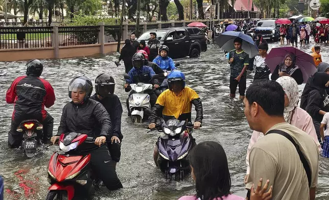 Motorist cross a flooded street after heavy monsoon rains in downtown Kota Bharu, Kelantan, Malaysia, Friday, Nov. 29, 2024. (AP Photo/Loo Kok Chong)