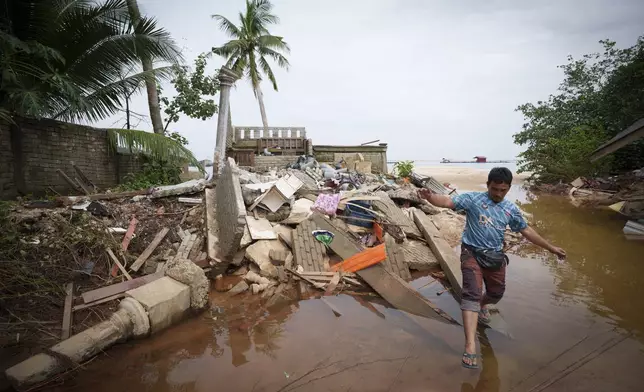 People wade through the water past a house damaged by flood in Tumpat, outskirts of Kota Bahru, Malaysia, Tuesday, Dec. 3, 2024. (AP Photo/Vincent Thian)