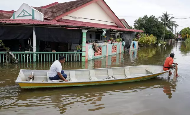 Men use a boat at a flooded neighborhood in Tumpat, on the outskirts of Kota Bahru, Malaysia, Tuesday, Dec. 3, 2024. (AP Photo/Vincent Thian)