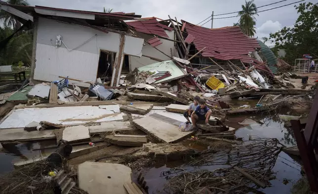 Children rest outside their house damaged by flood in Tumpat, on the outskirts of Kota Bahru, Malaysia, Tuesday, Dec. 3, 2024. (AP Photo/Vincent Thian)