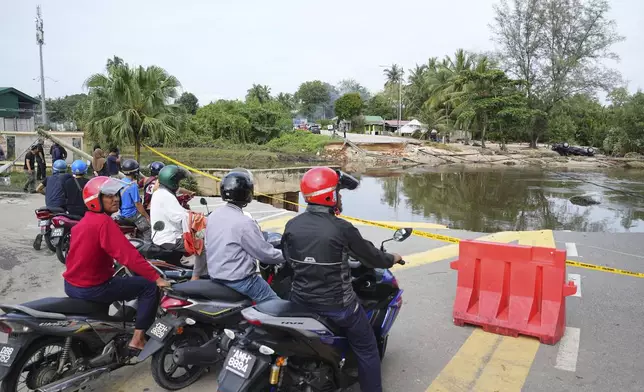 Motorists survey a road damaged by a flood in Tumpat, on the outskirts of Kota Bahru in Kelantan state on the east coast of Malaysia, Tuesday, Dec. 3, 2024. (AP Photo/Vincent Thian)