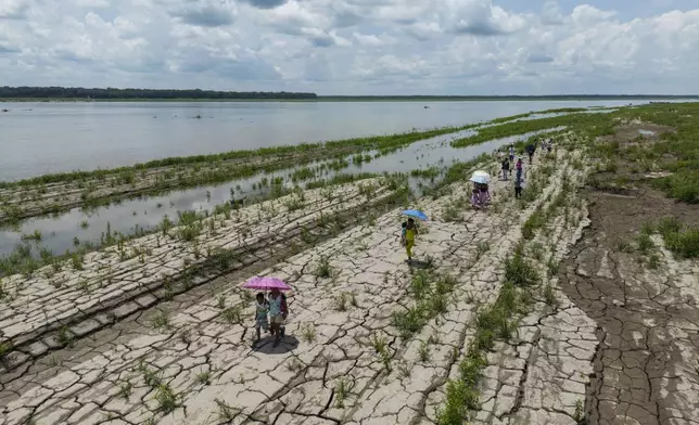 People walk through a part of the Amazon River that shows signs of drought in Santa Sofia, Colombia, Oct. 20, 2024. (AP Photo/Ivan Valencia)