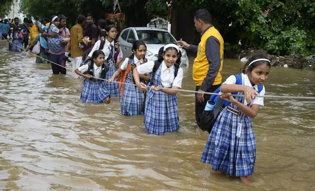 Students hold on to a rope as they cross a street flooded after heavy rains, on their way home in Ajmer, India, Sept. 6, 2024. (AP Photo/Deepak Sharma)