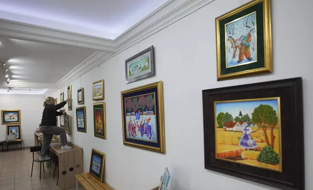 Klara Babka hangs a painting in the Gallery of naive art in the village of Kovacica, Serbia, Thursday, Nov. 28, 2024. (AP Photo/Darko Vojinovic)