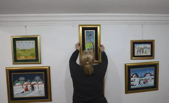 Klara Babka hangs a painting in the Gallery of naive art in the village of Kovacica, Serbia, Thursday, Nov. 28, 2024. (AP Photo/Darko Vojinovic)