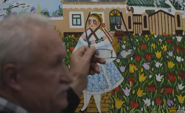 Pavel Babka, gallerist and naïve art expert shows painting of a girl in traditional Slovak multi-layered skirt in the village of Kovacica, Serbia, Thursday, Nov. 28, 2024. (AP Photo/Darko Vojinovic)