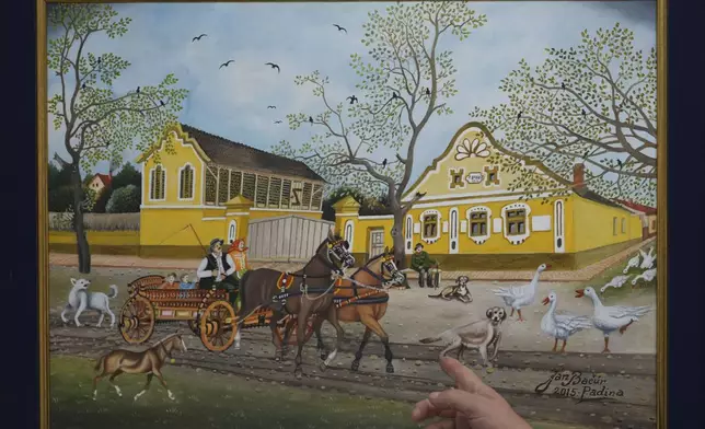 Pavel Babka, gallerist and naïve art expert shows painting of a horse-drawn cart and a yellow house dating back to Austro-Hungarian times in the village of Kovacica, Serbia, Thursday, Nov. 28, 2024. (AP Photo/Darko Vojinovic)