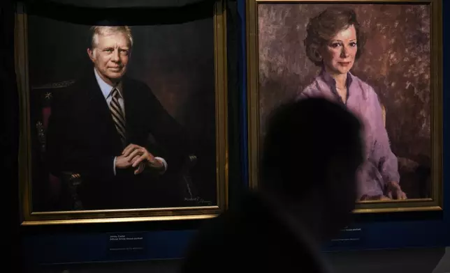 A man moves by the portrait of former President Jimmy Carter and his wife Rosalynn Carter at the Jimmy Carter National Historical Park, Monday, Dec. 30, 2024, in Plains, Ga. Jimmy Carter died Sunday at the age of 100. (AP Photo/Mike Stewart)