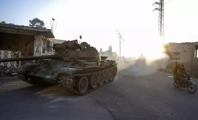 Syrian opposition fighters drive a motorcycle and an armoured vehicle seized from the Syrian army in the town of Maarat al-Numan, south of Idlib, Syria, Tuesday Dec. 3, 2024.(AP Photo/Omar Albam)