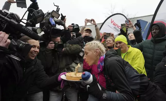 Belgian ultra runner Hilde Dosogne, center, blows out candles on a cake after crossing the finish line of her 366th consecutive marathon in Ghent, Belgium, Tuesday, Dec. 31, 2024. (AP Photo/Virginia Mayo)