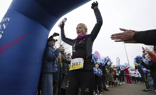 Belgian ultra runner Hilde Dosogne, center, is cheered on as she crosses the finish line during her 366th consecutive marathon in Ghent, Belgium, Tuesday, Dec. 31, 2024. (AP Photo/Virginia Mayo)