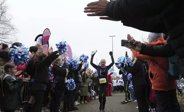 Belgian ultra runner Hilde Dosogne, center, is cheered on as she crosses the finish line during her 366th consecutive marathon in Ghent, Belgium, Tuesday, Dec. 31, 2024. (AP Photo/Virginia Mayo)