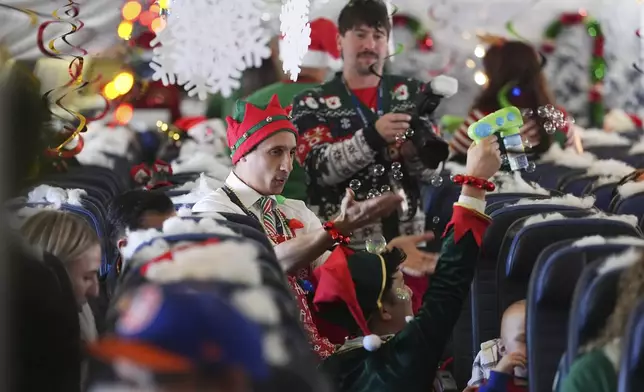 Flight attendant Gustavo Oliveira, center, juggles bubbles to entertain passengers during the United Airlines annual "fantasy flight" to a fictional North Pole at Denver International Airport, Saturday, Dec. 14, 2024, in Denver. (AP Photo/David Zalubowski)