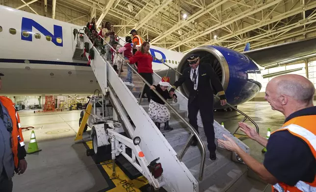 Captain Paul Purkey helps a participant navigate the stairs during the United Airlines annual "fantasy flight" to a fictional North Pole at Denver International Airport, Saturday, Dec. 14, 2024, in Denver. (AP Photo/David Zalubowski)