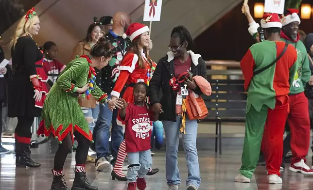 Flight attendant Dre Zulaica, front left, of San Francisco, greets a participant and her guardian during the United Airlines annual "fantasy flight" to a fictional North Pole at Denver International Airport, Saturday, Dec. 14, 2024, in Denver. (AP Photo/David Zalubowski)