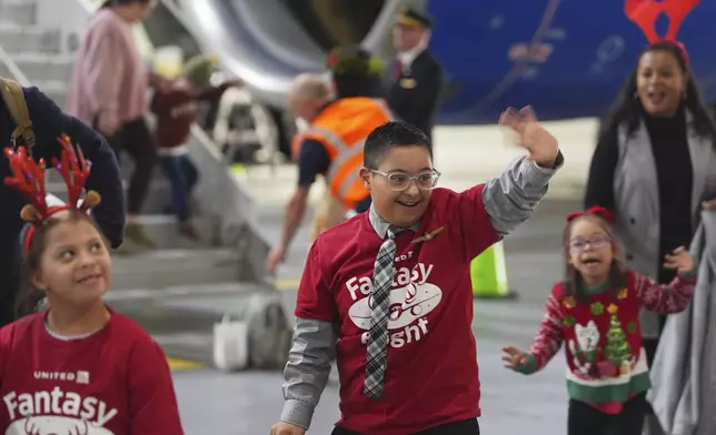 Twelve-year-old Adan Cervantes, center, of Denver, waves as he disembarks from a plane during the United Airlines annual "fantasy flight" to a fictional North Pole at Denver International Airport, Saturday, Dec. 14, 2024, in Denver. (AP Photo/David Zalubowski)