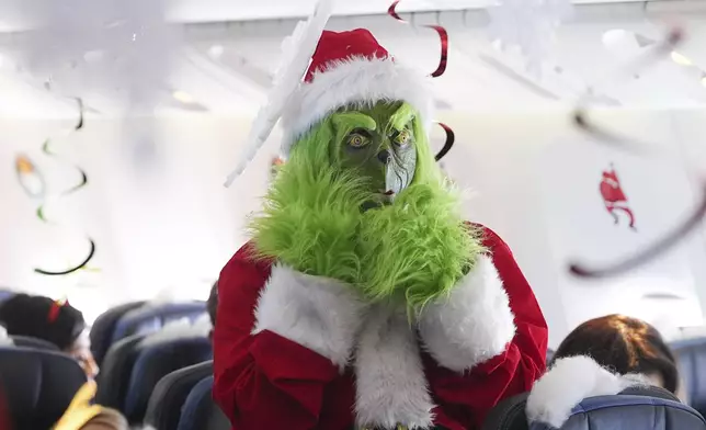 Dressed in a Grinch costume, a flight attendant entertains passengers during the United Airlines annual "fantasy flight" to a fictional North Pole at Denver International Airport, Saturday, Dec. 14, 2024, in Denver. (AP Photo/David Zalubowski)