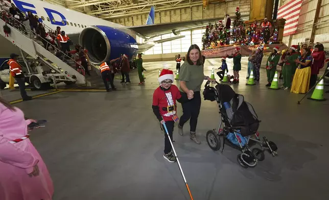 Nine-year-old Rylan Hadad, left, walks with his mother, Eva, during the United Airlines annual "fantasy flight" to a fictional North Pole at Denver International Airport, Saturday, Dec. 14, 2024, in Denver. (AP Photo/David Zalubowski)