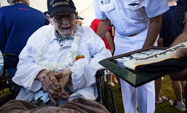 Pearl Harbor survivor Ira "Ike" Schab, 104, from Beaverton, Ore., looks at a photo presented by an attendee after the 83rd Pearl Harbor Remembrance Day ceremony, Saturday, Dec. 7, 2024, in Honolulu. (AP Photo/Mengshin Lin)