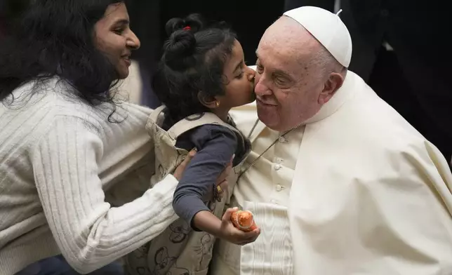 Pope Francis is kisses by a child during the weekly general audience at the Vatican, Wednesday, Dec. 18, 2024. (AP Photo/Alessandra Tarantino)