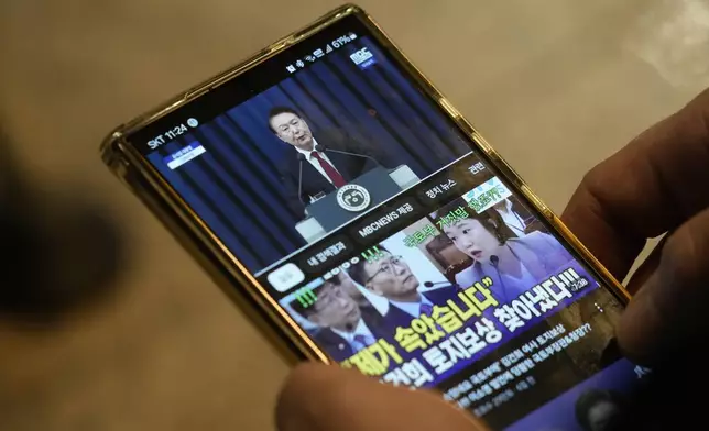 A man watches his smart phone showing South Korean President Yoon Suk Yeol's televised briefing at a bus terminal in Seoul, South Korea, Tuesday, Dec. 3, 2024. (AP Photo/Ahn Young-joon)