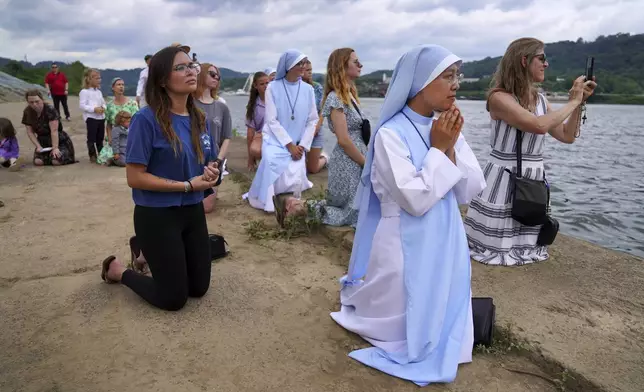 Sister Mary Fatima Pham, second from right, kneels with her fellow Catholics as they watch the Eucharist brought on board a boat on the Ohio River at the Steubenville Marina in Steubenville, Ohio, Sunday, June 23, 2024. The National Eucharistic Pilgrimage will conclude at the National Eucharistic Congress in Indianapolis in mid-July, the first held in more than 80 years. (AP Photo/Jessie Wardarski)