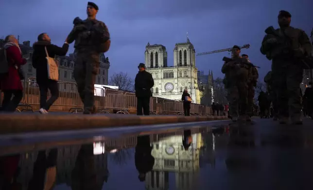 People walk past as France's iconic Notre Dame Cathedral is reflected in a puddle Saturday, Dec. 7, 2024 in Paris before the formal reopening for the first time since a devastating fire nearly destroyed the 861-year-old landmark in 2019. (AP Photo/Alessandra Tarantino)