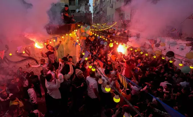 Residents of Ezbet Hamada in Cairo's El Matareya district light flares as the celebrate mass breakfast, "Iftar", the meal to end their fast at sunset, during the holy fasting month of Ramadan in Cairo, Egypt, Monday, March 25, 2024. (AP Photo/Amr Nabil)