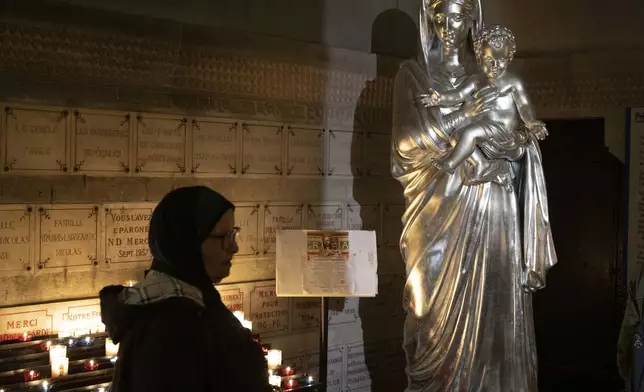 A Muslim woman walks by an icon of the Virgin Mary and Jesus at the Notre Dame de la Garde Basilica in Marseille, southern France, Friday, April 19, 2024. (AP Photo/Daniel Cole)