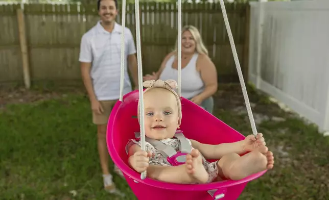 Sam Earle, left, and his wife, Tori, watch their daughter, Novalie, swing in their backyard Tuesday, May 7, 2024, in Lakeland, Fla. Novalie was born through an embryo adoption. "God can use everything to His glory," says Sam, 30. "There's certainly an aspect that you consider with IVF: the ethics of freezing more embryos than you need. … But for families who struggle with infertility, it's a beautiful opportunity." (AP Photo/Mike Carlson)