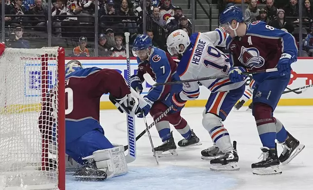 Edmonton Oilers center Adam Henrique, right center, redirects the puck at Colorado Avalanche goaltender Alexandar Georgiev, left, while driving between defensemen Devon Toews, back, and Cale Makar in the second period of an NHL hockey game, Saturday, Nov. 30, 2024, in Denver. (AP Photo/David Zalubowski)