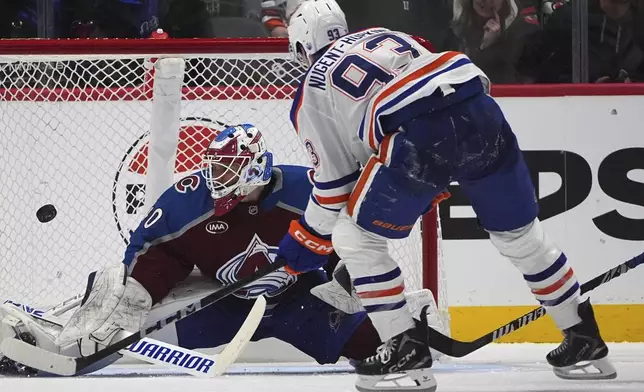 Edmonton Oilers center Ryan Nugent-Hopkins, front, puts a shot on Colorado Avalanche goaltender Alexandar Georgiev in the third period of an NHL hockey game Saturday, Nov. 30, 2024, in Denver. (AP Photo/David Zalubowski)