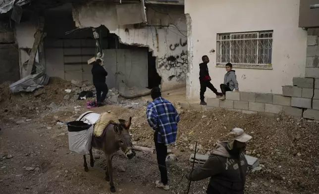 Locals stand next to a damaged building after the latest Israeli military operation, in the West Bank city of Tulkarem, Thursday, Dec. 26, 2024. (AP Photo/Matias Delacroix)