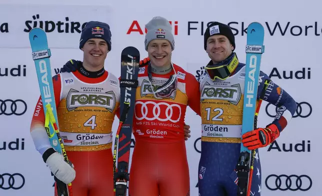 Switzerland's Marco Odermatt, center, winner of an alpine ski, men's World Cup downhill, celebrates on the podium with second-placed Switzerland's Franjo von Allmen, left, and third-placed United States' Ryan Cochran Siegle, in Val Gardena, Italy, Saturday, Dec. 21, 2024. (AP Photo/Alessandro Trovati)