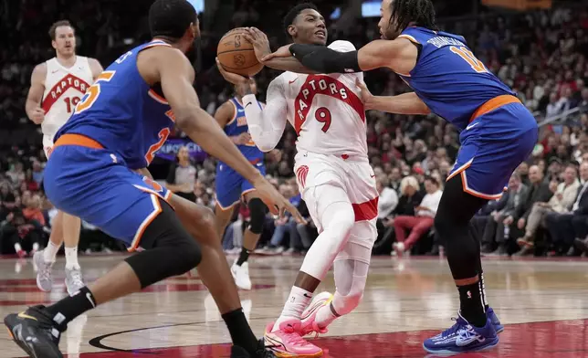 Toronto Raptors guard RJ Barrett (9) gets fouled by New York Knicks guard Jalen Brunson (11) as teammate Mikal Bridges (25) looks on during the first half of an NBA basketball game in Toronto, Monday, Dec. 9, 2024. (Nathan Denette/The Canadian Press via AP)