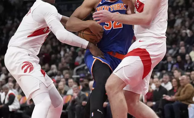 New York Knicks center Karl-Anthony Towns drives into Toronto Raptors center Jakob Poeltl as teammate Toronto Raptors guard RJ Barrett defends during the second half of an NBA basketball game in Toronto, Monday, Dec. 9, 2024. (Nathan Denette/The Canadian Press via AP)