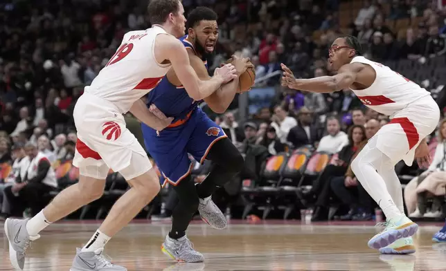 New York Knicks center Karl-Anthony Towns, center, drives between Toronto Raptors center Jakob Poeltl and teammate Scottie Barnes during the second half of an NBA basketball game in Toronto, Monday, Dec. 9, 2024. (Nathan Denette/The Canadian Press via AP)