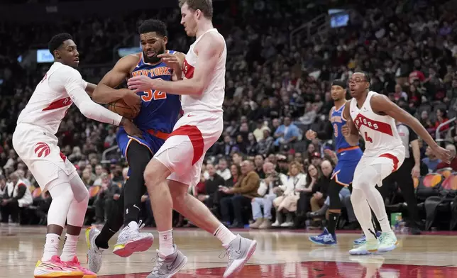 New York Knicks center Karl-Anthony Towns drives into Toronto Raptors center Jakob Poeltl as teammate Toronto Raptors guard RJ Barrett (9) defends during the second half of an NBA basketball game in Toronto, Monday, Dec. 9, 2024. (Nathan Denette/The Canadian Press via AP)