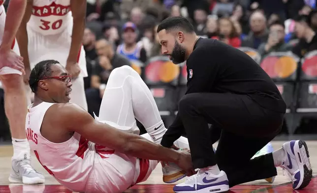 Toronto Raptors forward Scottie Barnes is tended to by a team trainer after getting hurt during the second half of an NBA basketball game against New York Knicks in Toronto, Monday, Dec. 9, 2024. (Nathan Denette/The Canadian Press via AP)