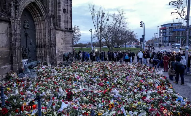 People lay flowers and lit candles in front of the Johannis church close to the Christmas market, where a car drove into a crowd on Friday evening, in Magdeburg, Germany, Sunday, Dec. 22, 2024. (AP Photo/Ebrahim Noroozi)