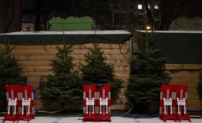 Mobile vehicle barriers sit behind stalls at the Christmas market on Rotkreuzplatz, early Monday, Dec. 23, 2024, in Munich. (Sven Hoppe/dpa via AP)