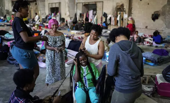 Sierra Leonean migrant workers stranded in Lebanon, work on their colleague's hair, as they wait to be repatriated back home, as they are sheltered at a former car dealership that was turned into a shelter in Hazmieh, east of Beirut, Lebanon, Friday, Nov. 15, 2024. (AP Photo/Hassan Ammar)