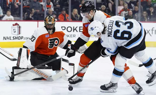Philadelphia Flyers goaltender Samuel Ersson, left, looks for the puck as Flyers' Travis Sanheim, center, and Utah Hockey Club's Matias Maccelli (63) battle during the first period of an NHL hockey game, Sunday, Dec. 8, 2024, in Philadelphia. (AP Photo/Derik Hamilton)